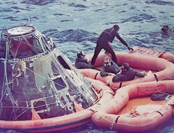 A photo of astronauts Mitchell,Shepard,and Roosa, and a frogman on a raft